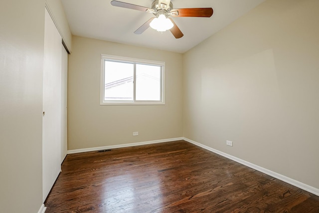 empty room with dark wood-style floors, a ceiling fan, visible vents, and baseboards