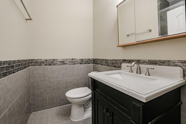 bathroom with toilet, wainscoting, tile walls, and vanity