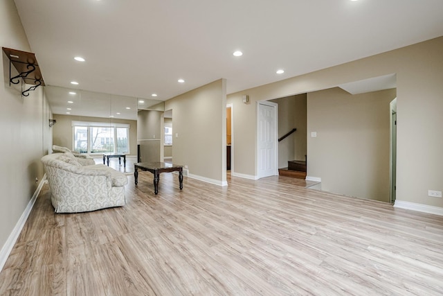 unfurnished living room with baseboards, light wood finished floors, stairway, and recessed lighting