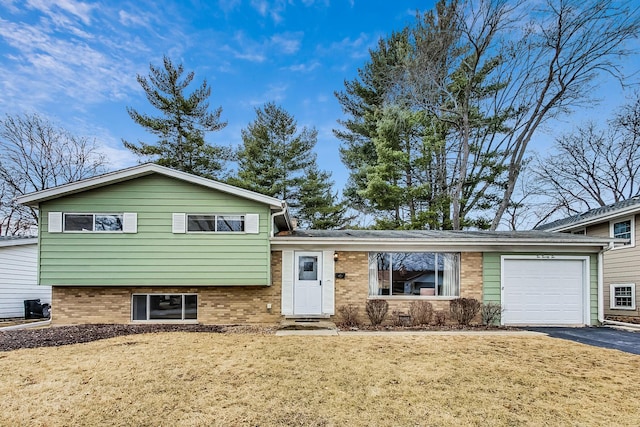 tri-level home featuring a garage, driveway, a front lawn, and brick siding