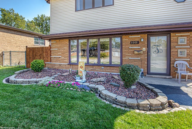 doorway to property with a yard, brick siding, and fence