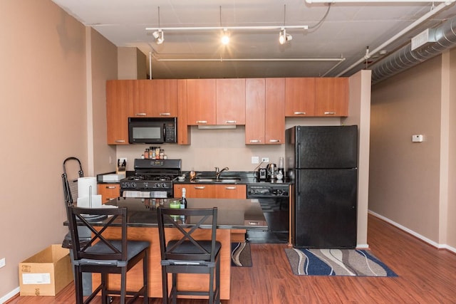 kitchen featuring baseboards, dark wood finished floors, dark countertops, black appliances, and a sink