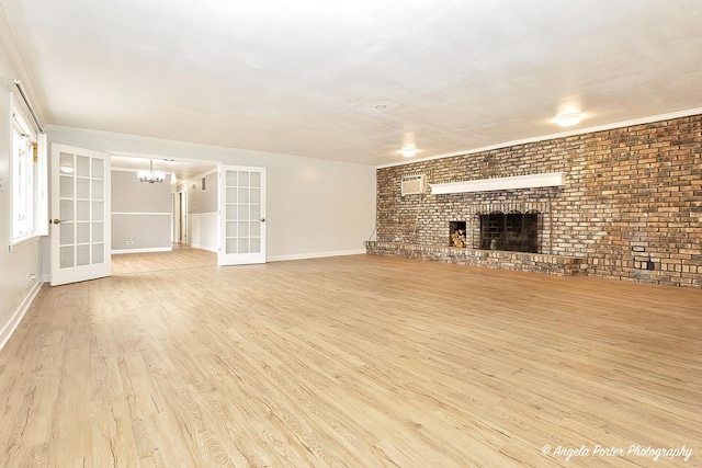 unfurnished living room with baseboards, brick wall, wood finished floors, an inviting chandelier, and a fireplace