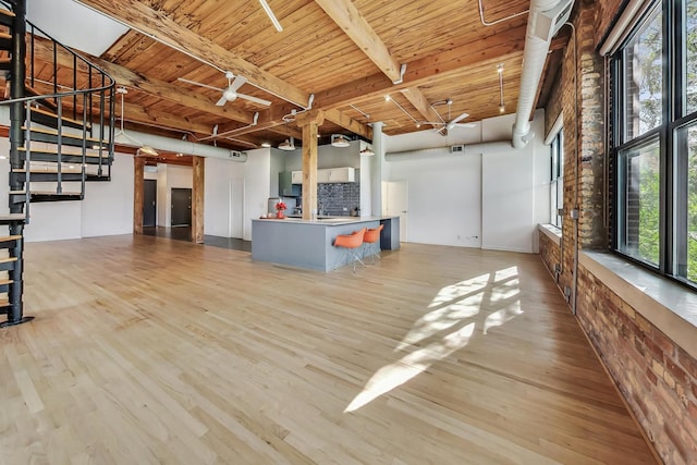 unfurnished living room with beam ceiling, light wood finished floors, stairway, a ceiling fan, and wood ceiling