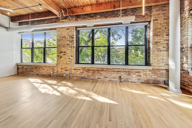 empty room featuring brick wall, beamed ceiling, wooden ceiling, and wood finished floors