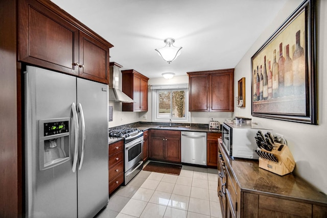 kitchen with light tile patterned floors, dark countertops, appliances with stainless steel finishes, a sink, and wall chimney exhaust hood