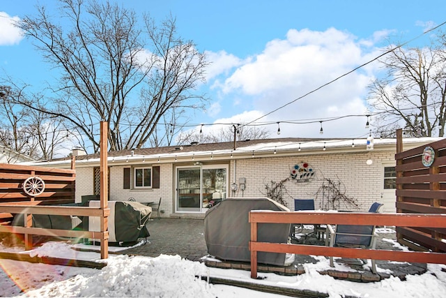 snow covered house featuring brick siding and fence