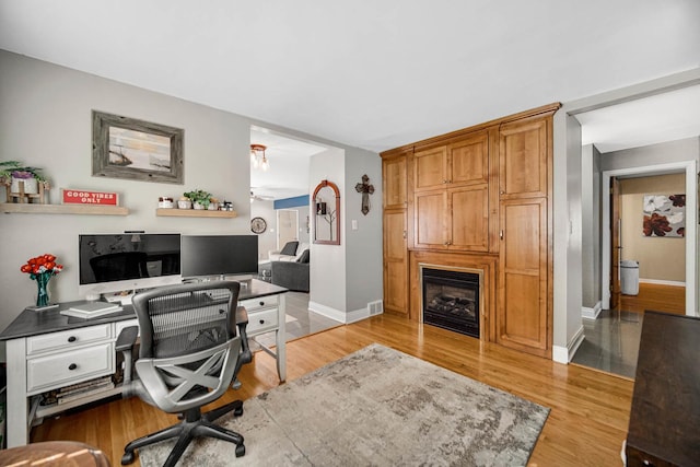 office area featuring a fireplace, light wood-style flooring, and baseboards