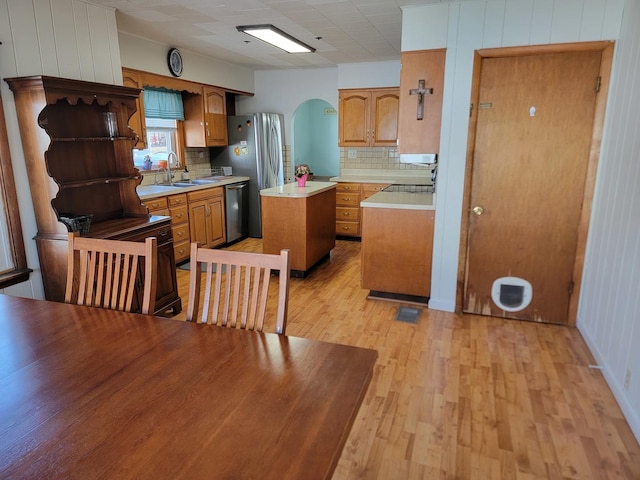 kitchen with light wood finished floors, arched walkways, brown cabinetry, a center island, and light countertops