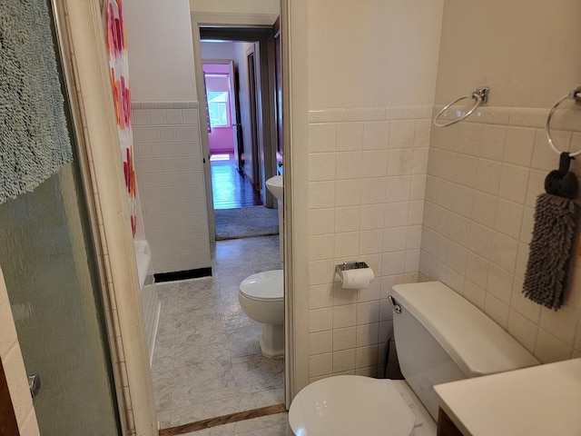 full bath featuring toilet, walk in shower, tile walls, and wainscoting