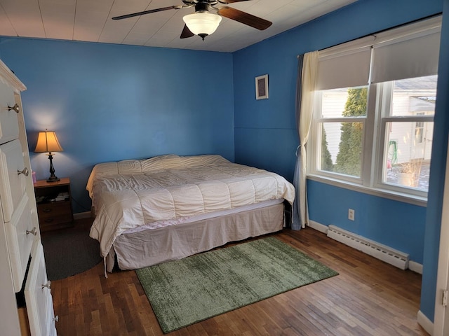 bedroom featuring a baseboard heating unit, ceiling fan, dark wood finished floors, and baseboards