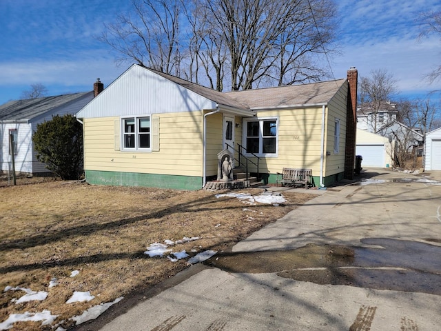 view of front of home featuring entry steps, a chimney, an outdoor structure, and a detached garage