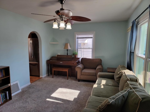 living area featuring arched walkways, carpet, visible vents, a ceiling fan, and baseboards