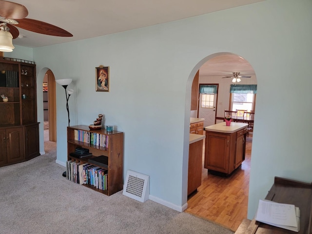 hallway with arched walkways, light carpet, visible vents, and baseboards