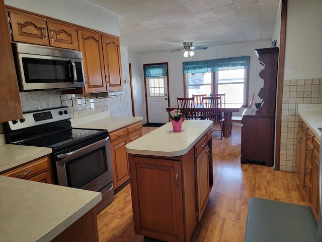 kitchen featuring brown cabinetry, a kitchen island, appliances with stainless steel finishes, and light countertops