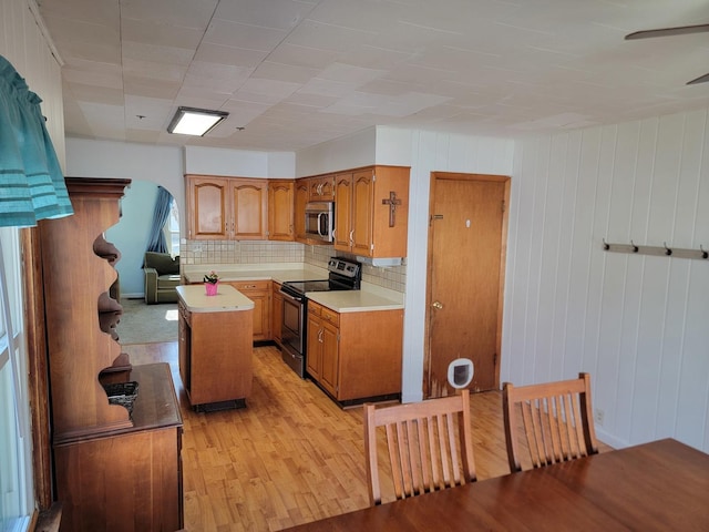 kitchen with stainless steel appliances, a kitchen island, light countertops, light wood-type flooring, and brown cabinets