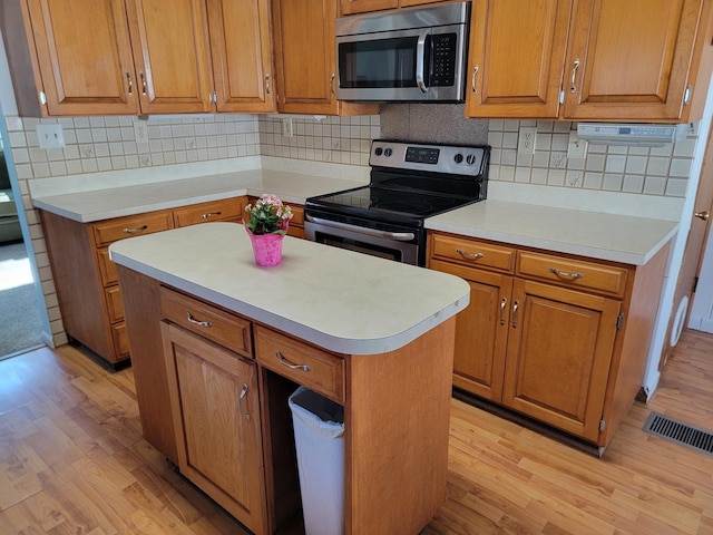 kitchen featuring light wood-style flooring, a kitchen island, light countertops, appliances with stainless steel finishes, and brown cabinets