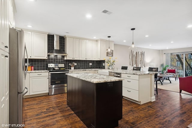 kitchen featuring wall chimney exhaust hood, appliances with stainless steel finishes, a kitchen island, and pendant lighting