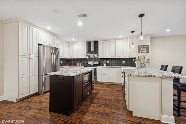 kitchen featuring wall chimney exhaust hood, a kitchen island, dark wood-style flooring, stainless steel appliances, and a kitchen bar