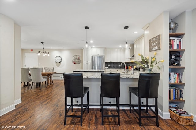 kitchen featuring light stone counters, decorative light fixtures, white cabinetry, a kitchen bar, and stainless steel refrigerator