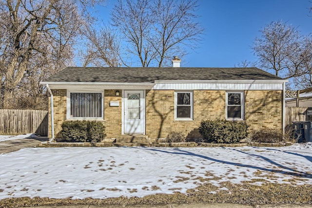 view of front of home with brick siding, a chimney, and fence