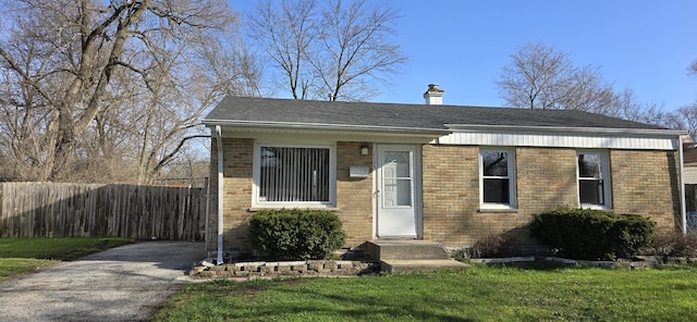 bungalow-style home with a chimney, fence, a front lawn, roof with shingles, and brick siding