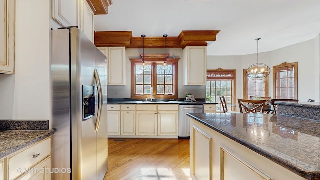 kitchen featuring appliances with stainless steel finishes, hanging light fixtures, cream cabinetry, light wood-type flooring, and a notable chandelier