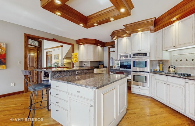 kitchen with light wood-style flooring, stainless steel appliances, a breakfast bar, decorative backsplash, and dark stone counters