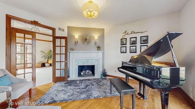 living area featuring french doors, a fireplace, visible vents, wood finished floors, and baseboards