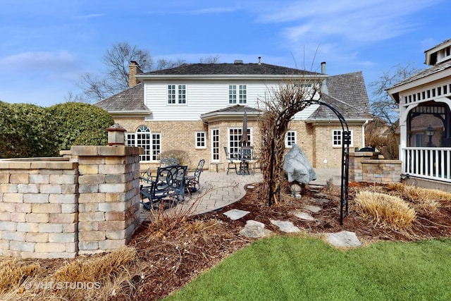 back of property with a patio area, brick siding, and a chimney