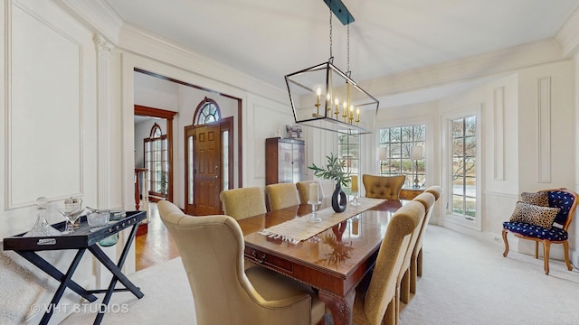 dining space with a chandelier, ornamental molding, a decorative wall, and light colored carpet