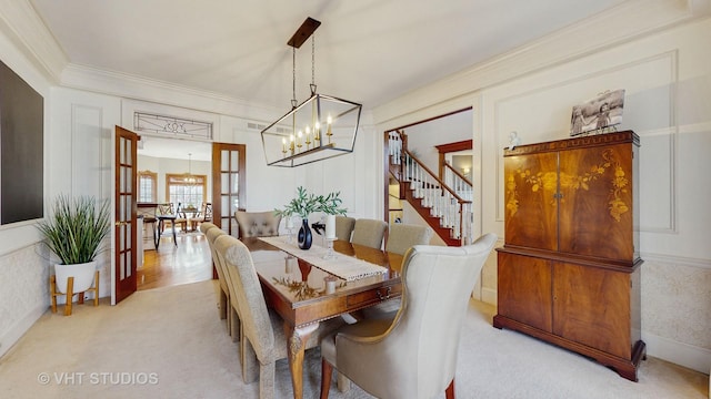 carpeted dining space with stairs, french doors, ornamental molding, and a decorative wall