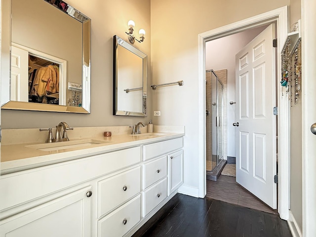 bathroom featuring double vanity, wood finished floors, a stall shower, and a sink