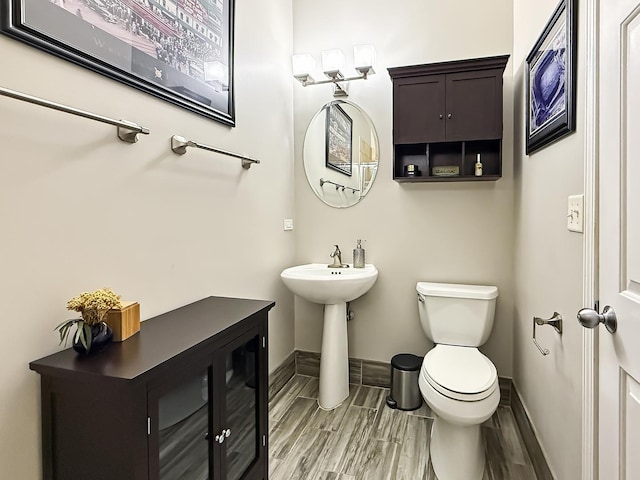 bathroom featuring toilet, wood tiled floor, baseboards, and a sink