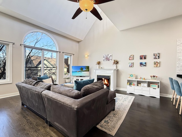 living area featuring a warm lit fireplace, high vaulted ceiling, dark wood finished floors, and baseboards