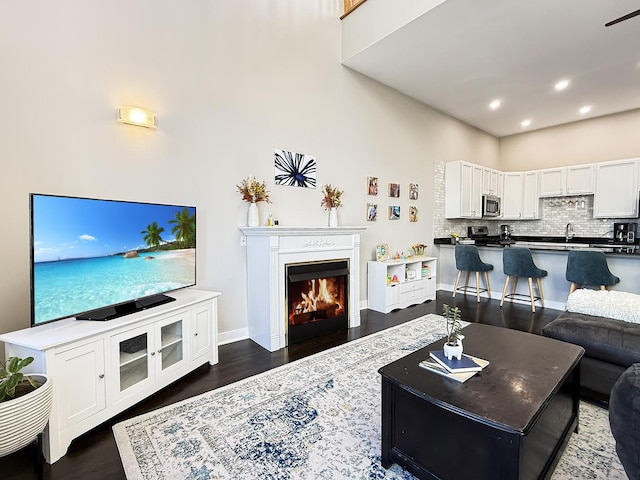 living area featuring a lit fireplace, dark wood-type flooring, recessed lighting, and baseboards