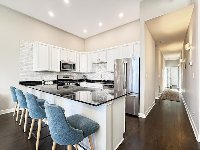 kitchen with dark wood-style floors, tasteful backsplash, appliances with stainless steel finishes, a peninsula, and a kitchen breakfast bar