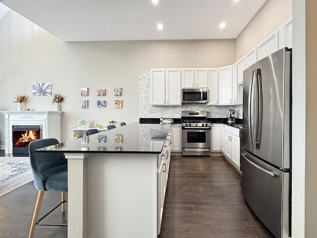 kitchen with stainless steel appliances, a warm lit fireplace, white cabinets, and tasteful backsplash