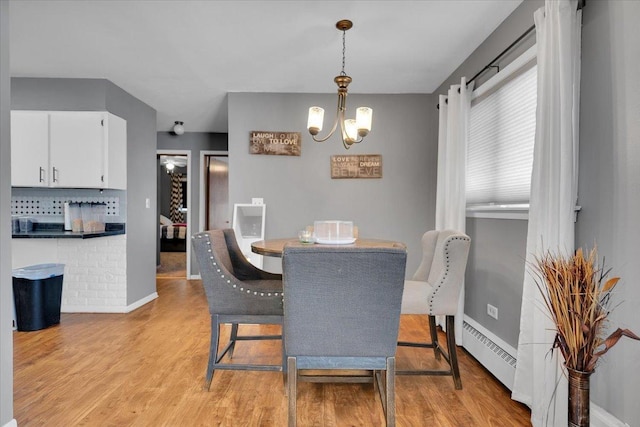 dining room with light wood-type flooring, a baseboard radiator, baseboards, and a notable chandelier