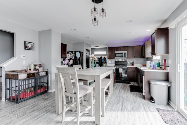 kitchen with dark brown cabinetry, baseboards, light countertops, light wood-type flooring, and black appliances