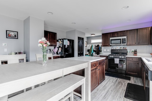 kitchen with light countertops, dark brown cabinetry, light wood finished floors, and black appliances