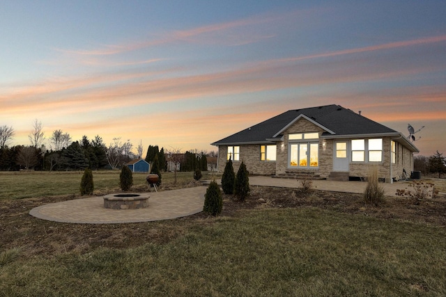 back of house at dusk with an outdoor fire pit, a patio, and a yard