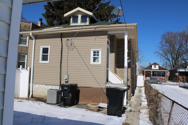 view of snow covered exterior featuring central AC and fence