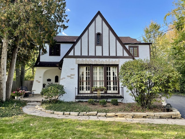 english style home featuring a patio, roof with shingles, fence, french doors, and stucco siding