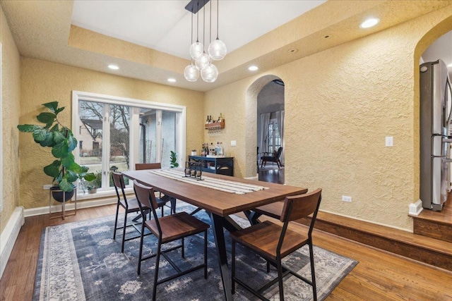 dining space featuring arched walkways, a textured wall, recessed lighting, wood finished floors, and a raised ceiling