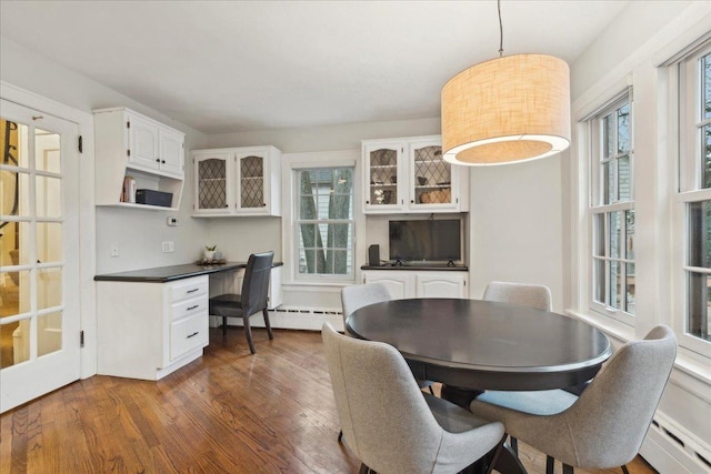 dining space featuring dark wood-type flooring, a baseboard heating unit, and built in desk