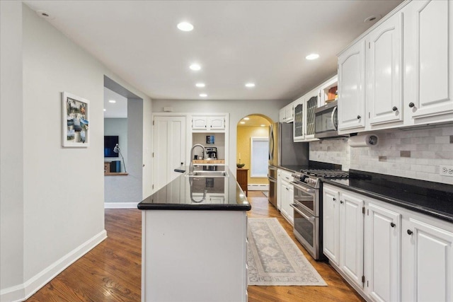 kitchen with arched walkways, dark countertops, wood finished floors, stainless steel appliances, and a sink