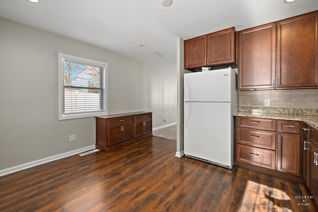 kitchen with dark wood-style floors, light stone counters, tasteful backsplash, freestanding refrigerator, and baseboards