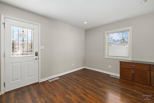 foyer entrance with dark wood-style floors, a healthy amount of sunlight, visible vents, and baseboards