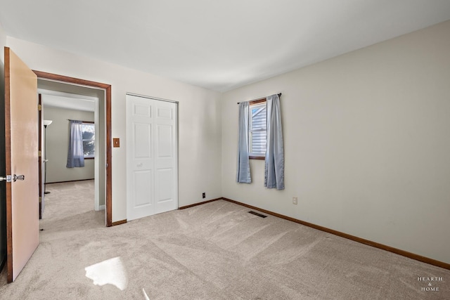 unfurnished bedroom with visible vents, baseboards, a closet, and light colored carpet